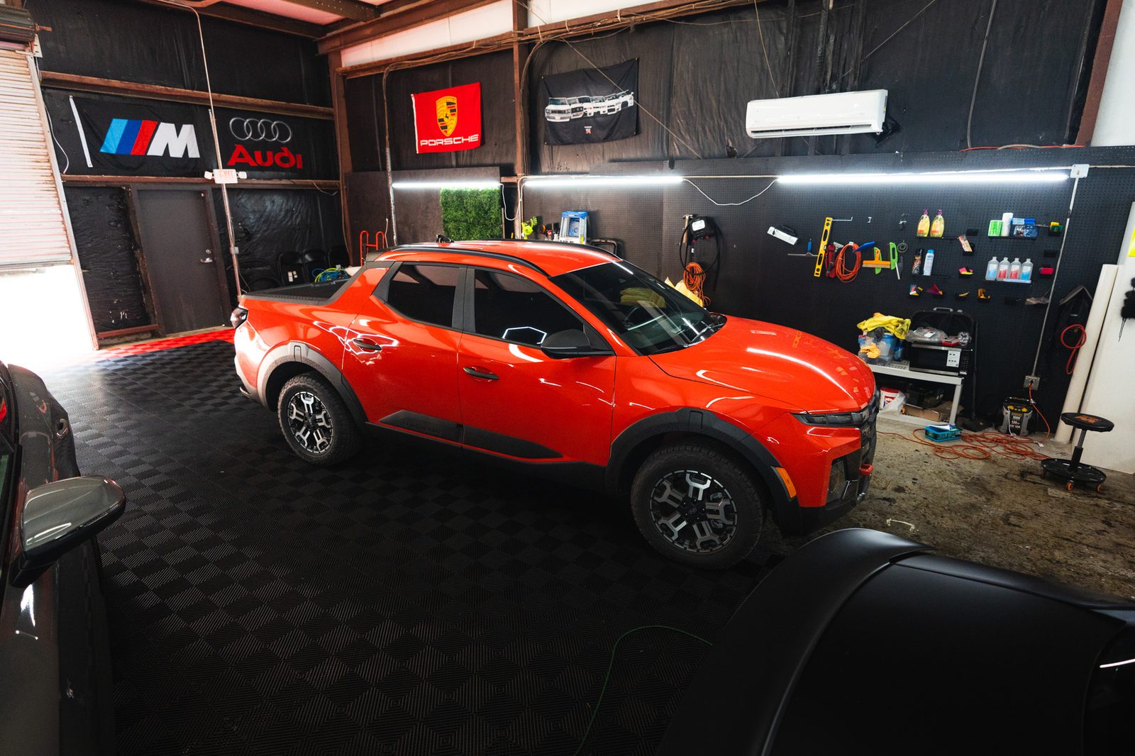 A red Hyundai Santa Cruz under the shop's hex lights